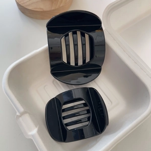 Close-up of two glossy black hair claw clips with hollowed-out stripe design on a tray