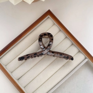 Detailed close-up of leopard print hair claw clip with golden metal spring on white tray