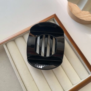 Detail view of glossy black circular hollow hair claw clip on soft beige velvet display
