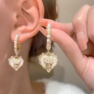 Close-up of pearl heart pendant earring with flower design on a model ear