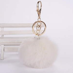 Detail of a white faux fur pompom keychain with a sparkling crystal ball and gold lobster clasp