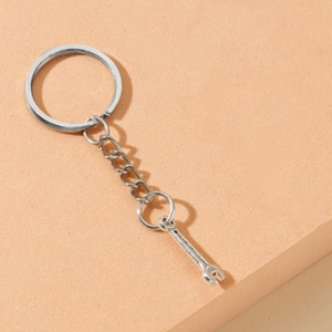 Close-up of a silver metal wrench keychain on a light orange textured surface