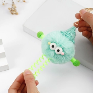 Detail of mint green plush monster keychain with spring legs and a knitted hat