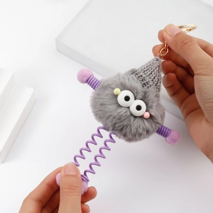 Close-up of grey plush monster keychain with stretchable purple spring legs and gold ring