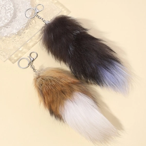 Detail showing two plush faux fur fox tail keychains in yellow and black on a warm beige base