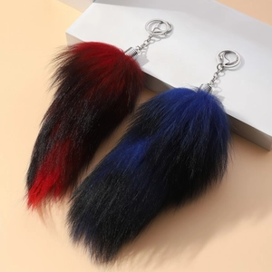 Close-up of red and blue faux fox tail keychains with silver metal hardware on a display pedestal
