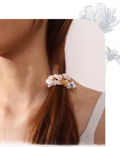 Close-up of beige pleated scrunchie with pearl, star, and ceramic bead pendant charms