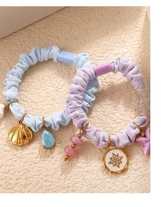 Close-up of pastel pleated scrunchies with shell and star pendants on a textured surface