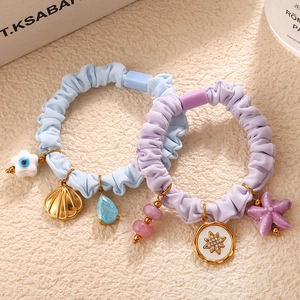 Pastel macaron scrunchies set with ocean charms including shells and starfish on beige surface