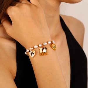 Bracelet en perles avec pendentifs chien et cœur dorés porté au poignet d'un modèle