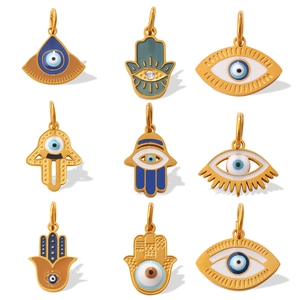 Gold Hamsa and Evil Eye pendants with blue enamel and crystal insets on white backdrop