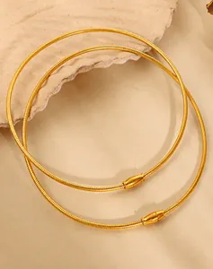 Detail of two layered gold snake chain necklaces with polished cylindrical clasps on sand