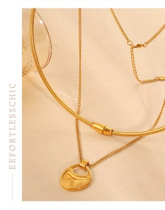 Detail of layered gold snake chain and geometric hollow pendant on warm textured background