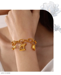 Close-up of gold chain bracelet with coin, heart and wolf charms worn on wrist