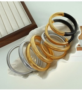 Close-up of stacked snake bone flexible metal bracelets in gold, silver, and black finishes
