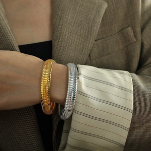Polished silver and gold Tubogas snake chain bracelets on a model wearing a brown blazer