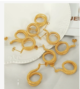 Dettaglio degli orecchini a forma di serpente dorati con trama a scaglie su ceramica