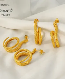 Dettaglio di orecchini a forma di serpente dorati con trama a scaglie su seta bianca