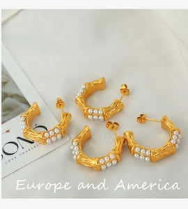 Macro detail of C-shaped bamboo texture earrings with pearls on white fabric