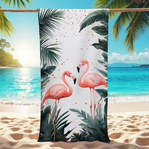 Microfiber beach towel with pink flamingos and tropical palm leaves on a sunny beach