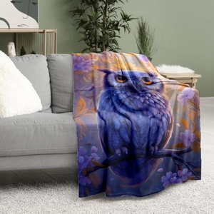 Purple owl and floral print flannel blanket draped over a grey fabric sofa in a cozy room