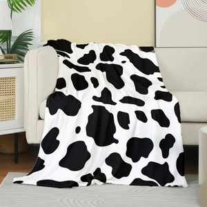 Weiche Flanelldecke mit Kuhmuster auf einem beigen Sofa in moderner Wohnzimmer-Deko
