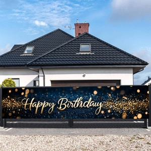 Dettaglio di uno striscione Happy Birthday blu e oro appeso a una recinzione nera da giardino