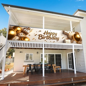 Golden balloon birthday banner hanging on a white terrace balcony against blue sky