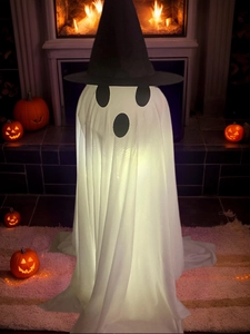 Close-up of glowing Halloween ghost decor with black wizard hat near a warm fireplace