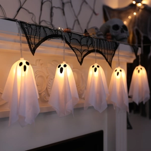 Detail of five glowing white fabric ghost LED string lights on a decorated fireplace mantel