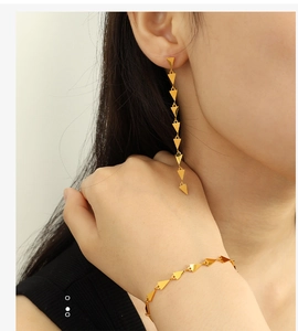 Detail of minimalist golden geometric triangle drop earrings and matching chain bracelet set