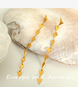 Detail of long golden tassel earrings with geometric triangle elements on shell