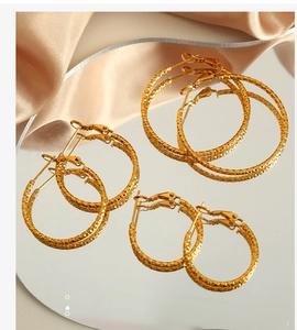 Drei Paar goldene Creolen mit Diamantschliff-Textur auf einer spiegelnden Fläche