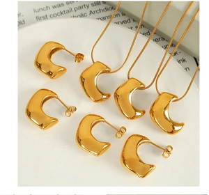 Detailed view of polished 18K gold C-shape earrings and horn pendant on a marble plate