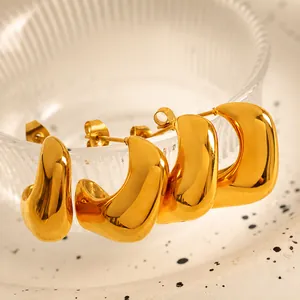 Macro shot of gold-plated chunky C-shape hoop earrings hanging on textured glass