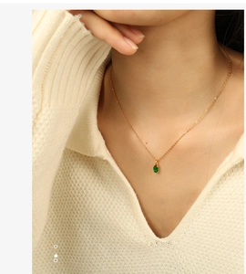 Detailed close-up of a delicate gold chain necklace with a green oval gemstone on a model