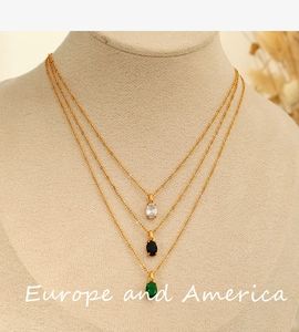 Close-up of triple-layered gold necklace featuring clear, black and green oval crystals