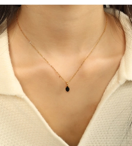 Detail of elegant gold necklace featuring a minimalist oval black gemstone pendant