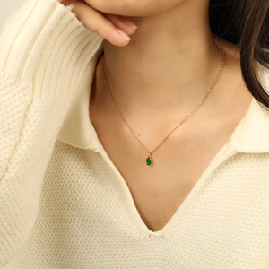Minimalist gold necklace with an oval emerald green zircon pendant worn on a female neck