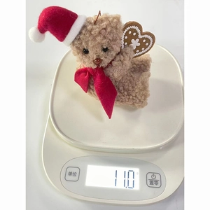 Detail shot showing a lightweight 11.0g plush teddy bear charm with a festive hat on a scale
