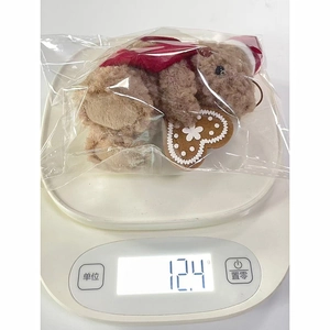 Macro view of a small brown teddy bear with a Christmas hat weighing 12.4g on a digital scale
