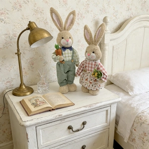 Pair of Easter bunny plush dolls in rustic outfits on a cozy bedside table decor