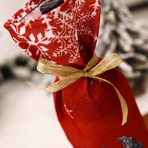 Christmas burlap wine gift bag with white snowflake print and golden ribbon bow on bottle