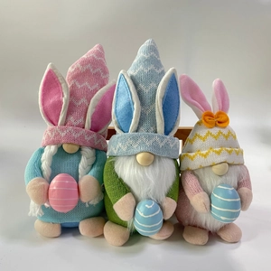 Detalle de tres gnomos de Pascua de felpa con orejas de conejo y huevos coloridos