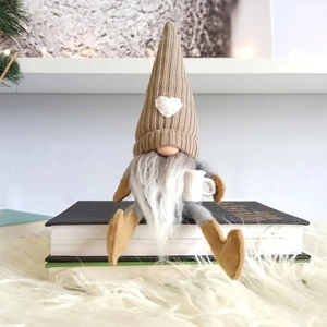 Gestrickter Weihnachtsgnom mit Kaffeetasse und Herzflicken auf gemütlichem Hintergrund