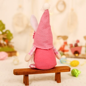 Pink Easter gnome plush with bunny ears and knit hat sitting on a rustic wooden bench