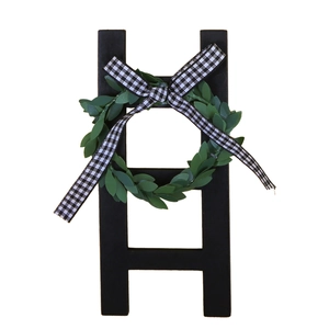 Détail d'une mini échelle rustique noire en bois avec couronne verte et nœud à carreaux