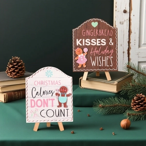 Close-up of wooden gingerbread signs with holiday text and easel stands on green desk