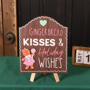 Close-up of wooden Gingerbread Kisses holiday sign with mini tripod stand on green surface