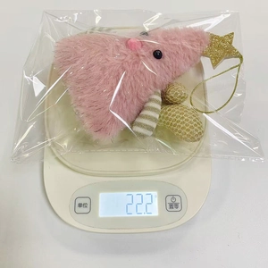 Detail showing a pink plush Christmas tree ornament on a scale weighing 22.2 grams